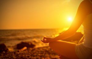 hand of  woman meditating in a yoga pose on beach at sunset