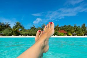 Close-up of female foot in the blue water on the tropical beach.