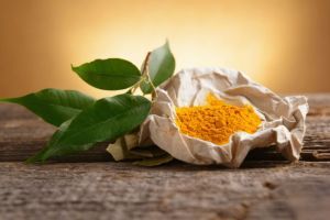 Tumeric powwder spice on wooden board with fresh leaves