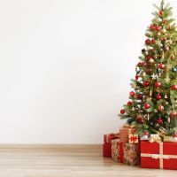 Big beautiful christmas tree decorated with beautiful shiny baubles and many different presents on wooden floor. White wall background with a lot of copy space for text. Close up.
