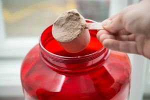 Man taking protein from container by the scoop.