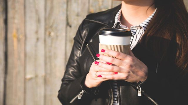 Paper cup with coffee in hand at the girl