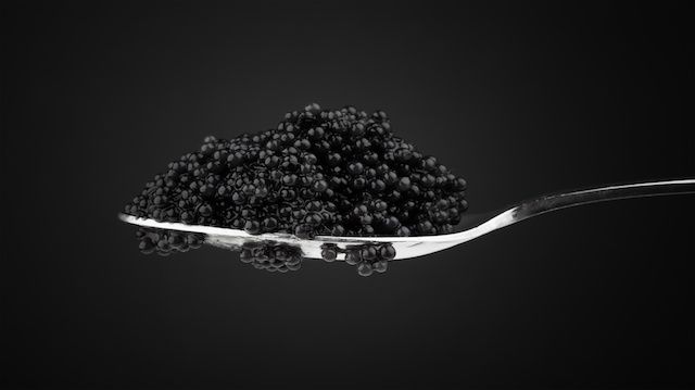 Black caviar in metal teaspoon. Macro photo on dark background