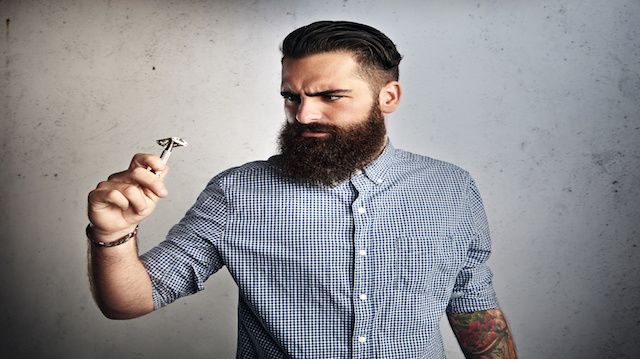 Portrait of brutal bearded man looking at vintage razor