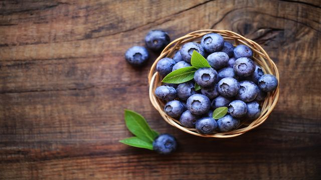 Fresh ripe garden blueberries in a wicker bowl on dark rustic wooden table. with copy space for your text