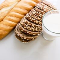 Glass of milk and bread placed on a white table.