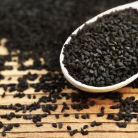 Black cumin (nigella sativa or kalonji) seeds in spoon on wooden background