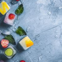 Ice cubes with fruit and broken ice on a stone blue background with mint leaves and fresh fruit. Mint, strawberry, cherry, lemon, orange. Flat lay, top view