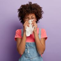 Portrait of sick African American woman sneezes in white tissue, suffers from rhinitis and running nose, has allergy on something, looks unhealthy, feels unwell. Symptoms of cold or allergy.