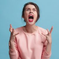 The young emotional angry woman screaming on blue studio background