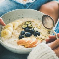 Woman in jeans and sweater eating healthy oatmeal porriage