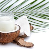 ripe coconut and organic coconut oil in glass jar with coconut leaf isolated on white