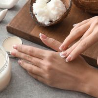 Woman applying coconut oil onto skin on grey background