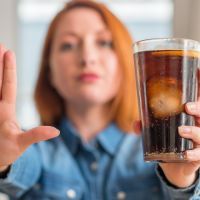 Redhead woman holding soda refreshment with open hand doing stop sign with serious and confident expression, defense gesture