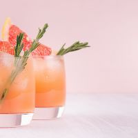 Summer cold cocktail with ice cubes, juice and slices grapefruit on pastel pink background.